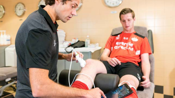 Medizinische Fachkraft beim Einsatz des Handheld-Ultraschallger&auml;ts am Knie eines Sportlers