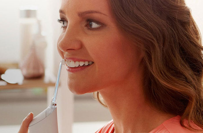 Eine Frau schaut gerade aus und putzt ihre wei&szlig;en Z&auml;hne mit einem Philips Sonicare Airfloss.